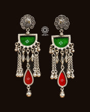Expertly crafted from 92.5 sterling silver, these Rang Mahal earrings feature a vibrant blend of green and red hues. With a peacock stud design, they effortlessly combine glass and silver to create a stunning pop of color. Make a bold statement with these beautiful, handcrafted earrings that are sure to become a favorite in your collection.