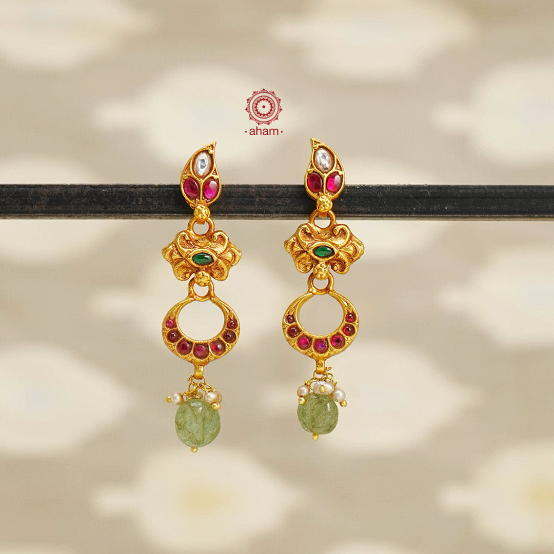 These South Indian style earrings are crafted in silver with a stunning dull gold polish. The kemp stone highlights and beautiful green drop with pearls add a touch of elegance. Simple yet striking, these earrings are perfect for any occasion.