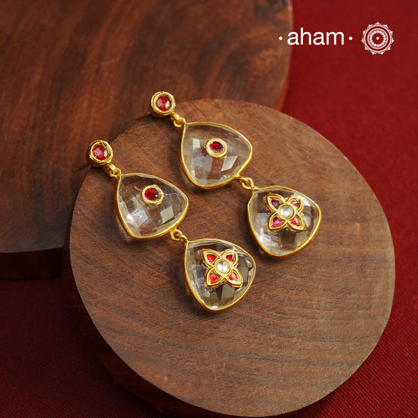 These Clear Quartz Gold Polish Silver Earrings are set in silver and feature exquisite kundan inlay work, blending traditional craftsmanship with contemporary style. Perfectly suited for Indo-Western ensembles, they add a touch of elegance and sophistication to your look. Crafted with attention to detail, these earrings enhance your outfit with their red stone contrast and subtle gold polish, making them a versatile accessory for special occasions.