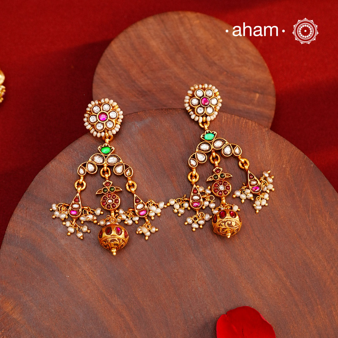 These Festive Gold Polish Silver Earrings feature traditional craftsmanship from South India in a modern design. Made with 92.5 silver, these earrings are adorned with kemp work and pearls, giving them a touch of elegance. Dipped in gold polish for added luster.