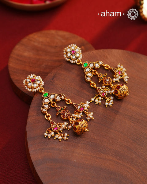 These Festive Gold Polish Silver Earrings feature traditional craftsmanship from South India in a modern design. Made with 92.5 silver, these earrings are adorned with kemp work and pearls, giving them a touch of elegance. Dipped in gold polish for added luster.