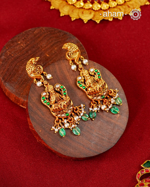 A celebration of prosperity, beauty, and traditional craftsmanship, these handcrafted earrings are crafted in 92.5 sterling silver and finished with a rich gold polish. The design features Goddess Lakshmi seated on a blooming lotus, symbolising abundance and good fortune, while intricately sculpted peacock motifs crown the earrings, representing grace, beauty, and renewal.

