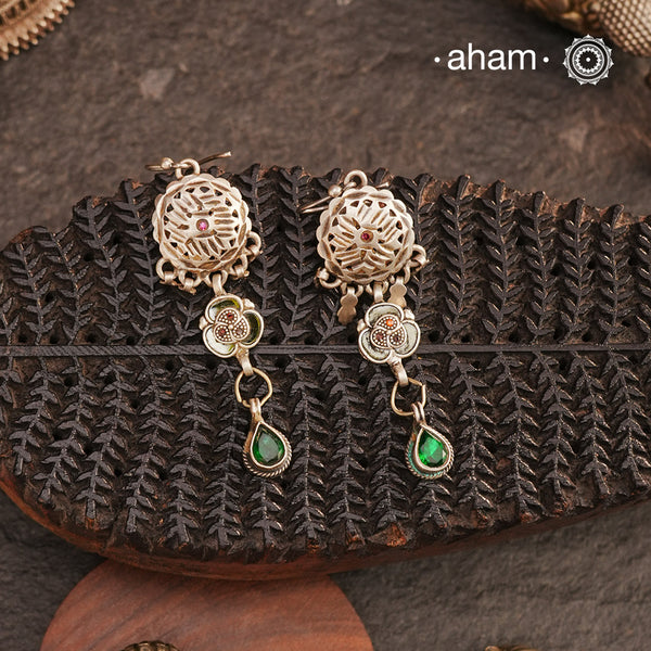 A unique creation from assorted tribal treasures, these Tribal Green Glass Silver Earrings feature a die-cut flower top with chilai work—once an earplug—followed by a smaller flower and a striking green glass drop. The added fishhook ensures ease of wear. Handcrafted in pure silver, this pair beautifully reflects the artistry of traditional tribal jewellery.