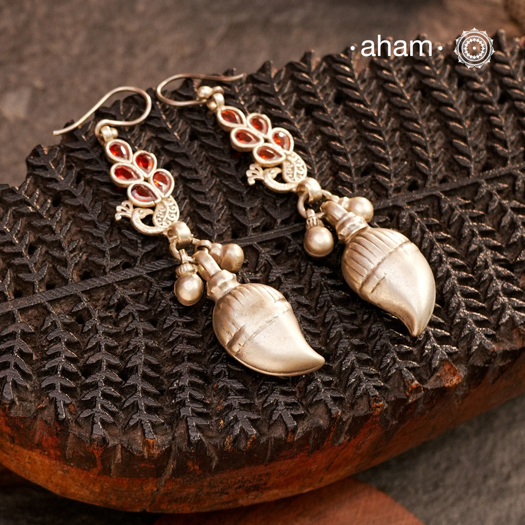 Celebrate timeless tradition with our Tribal Ambi Silver Earrings, featuring a striking Ambi (Mango) bead adorned with delicate ghungroos at the bottom. The top showcases beautiful peacocks with red glass. Handcrafted in silver, these earrings embody the beauty of vintage tribal jewellery — perfect for those seeking a blend of heritage and charm.