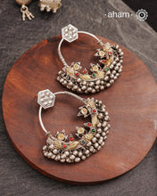 A classic design from Rajasthan's tribal heritage, these Tribal Silver Bali Earrings feature a delicate curve adorned with red and green stones and a cluster of ghungroos at the bottom, adding rhythm and movement. We have added a hook on the top for ease of wear. Handcrafted in silver, these balis perfectly capture the essence of traditional tribal jewellery. Please note the earrings are sightly heavy.