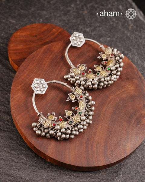 A classic design from Rajasthan's tribal heritage, these Tribal Silver Bali Earrings feature a delicate curve adorned with red and green stones and a cluster of ghungroos at the bottom, adding rhythm and movement. We have added a hook on the top for ease of wear. Handcrafted in silver, these balis perfectly capture the essence of traditional tribal jewellery. Please note the earrings are sightly heavy.