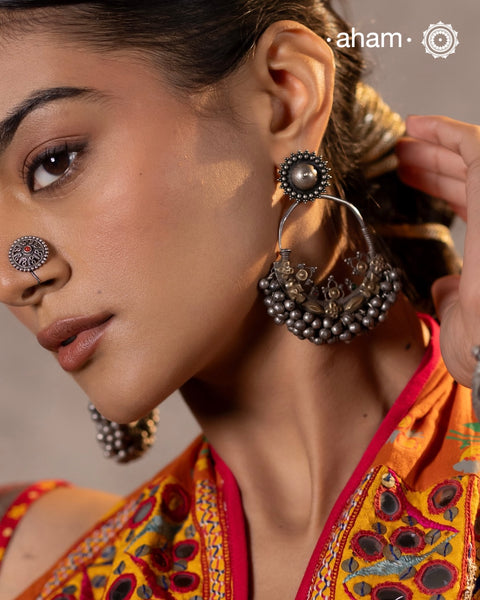 A classic design from Rajasthan's tribal heritage, these Tribal Silver ChandBali Earrings feature a delicate curve adorned with a cluster of ghungroos at the bottom, adding rhythm and movement. To enhance comfort and style, we’ve attached a flower stud at the top for easy wear. Handcrafted in silver, these balis perfectly capture the essence of traditional tribal jewellery.