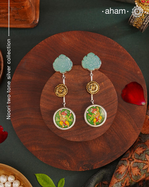 These Noori Two Tone Ganesha Silver Earrings feature a delicate two tone design, adorned with a hand painted miniature ganesha. Made from high quality 92.5 silver, these earrings are both stylish and unique. Elevate your look with the spiritual and cultural significance of these beautifully crafted earrings.