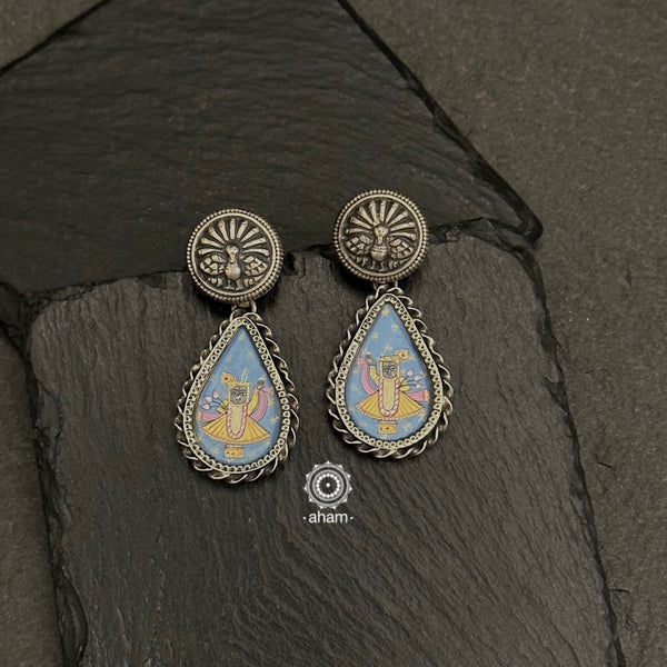 92.5 Silver earrings with intricate miniature hand painted Shrinathji motif in vibrant colours. Enclosed with a glass top, these are hand painted one of a kind wearable art pieces. 