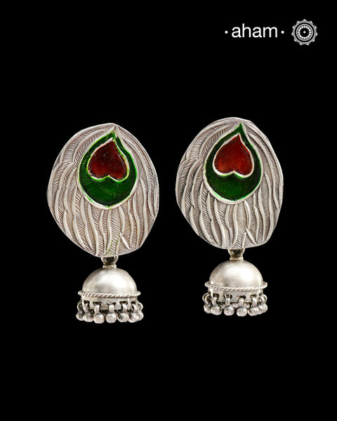 Exquisite peacock leaf studs adorned with intricate meena work, paired with graceful silver jhumkies that dance with every movement. The piece showcases masterful craftsmanship, combining traditional artistry with contemporary design. Handcrafted in pure silver, these earrings are a testament to refined taste and timeless sophistication.