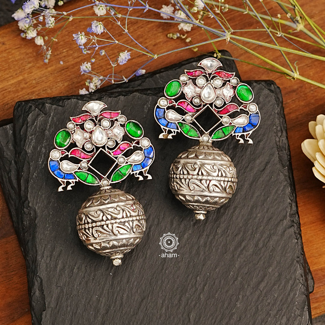 These Ira Peacock Drop Silver Earrings feature exquisite kundan work with a peacock motif, perfect for parties and evening soirees. Their lightweight ball drop construction ensures a comfortable fit. Elevate your outfit with this stunning piece of jewellery.