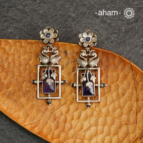 Elevate your style with our Ira Double Peacock Silver Earrings. These stylish earrings feature a stunning purple stone, surrounded by intricate peacock designs crafted in 92.5 silver. Add a touch of elegance to any outfit with these beautiful earrings.