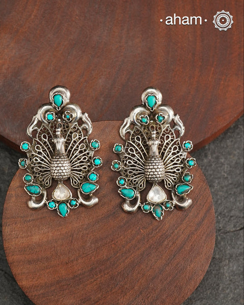Experience the majestic beauty of the peacock with our Ira Peacock Silver Earrings. Crafted in 92.5 silver and highlighted with turquoise stones, these earrings showcase the intricate details of this magnificent bird. Elevate your style and add a touch of nature-inspired elegance to your wardrobe.
