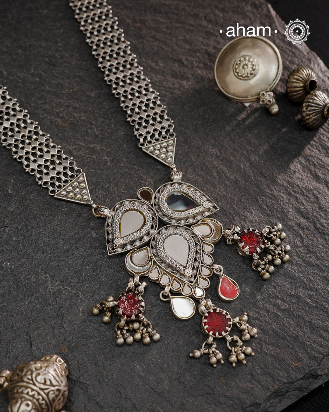 This Mewad White Glass Silver Neckpiece showcases a beautifully crafted glass pendant made by skilled karigars in Barmer, accented with vintage red glass drops. Complemented by elegant silver side bands, it reflects exquisite craftsmanship and adds a graceful, timeless charm to your jewelry collection.