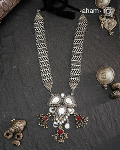 This Mewad White Glass Silver Neckpiece showcases a beautifully crafted glass pendant made by skilled karigars in Barmer, accented with vintage red glass drops. Complemented by elegant silver side bands, it reflects exquisite craftsmanship and adds a graceful, timeless charm to your jewelry collection.