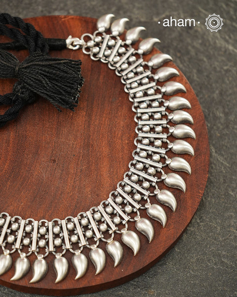 Crafted in 92.5 sterling silver, this handcrafted neckpiece is distinguished by its rhythmic arrangement of finely detailed silver bars, rava work, and elegant mango drops. The repeating motifs create a graceful silhouette that beautifully frames the neckline while showcasing the artistry of traditional silver craftsmanship.

Lightweight yet striking, this versatile piece effortlessly complements festive attire as well as everyday ensembles. Whether paired with a handloom saree, a classic kurta, or a contem