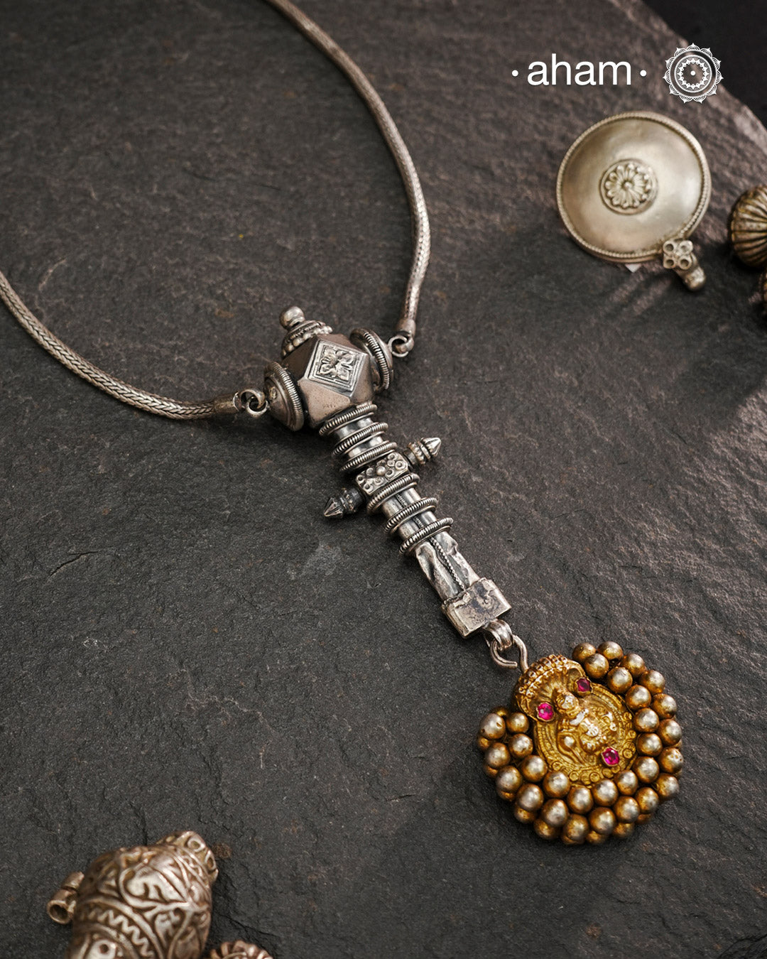 This Krishna Tribal Silver Neckpiece is a unique creation combining a vintage belt buckle and a vintage Krishna hair pin into a distinctive pendant. Expertly crafted in silver and finished with a woven chain, it offers a rare blend of heritage elements and artisanal craftsmanship, making it a remarkable statement piece for collectors and connoisseurs of fine jewellery.
