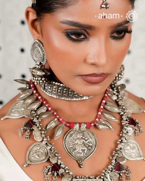 This Vintage Kal Bhairav Silver Neckpiece features a traditional central pendant symbolizing Kal Bhairav, flanked by bud-shaped beads on either side. Threaded on red cotton, it combines heritage craftsmanship with comfortable wear. Each piece reflects timeless artistry, offering a unique connection to history and culture for discerning collectors and enthusiasts.