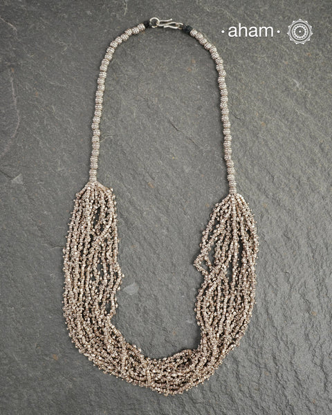 The Odhisa Dhaan Mala Silver Neckpiece is a masterful vintage creation featuring multiple strands of delicately crafted rice-shaped silver beads. Each bead is meticulously formed, reflecting exceptional craftsmanship rooted in Odisha’s rich heritage. This intricate neckpiece offers a timeless elegance, perfect for those who appreciate artisanal detail and cultural artistry in their jewellery collection.