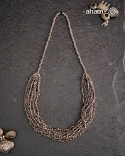 The Odhisa Dhaan Mala Silver Neckpiece is a masterful vintage creation featuring multiple strands of delicately crafted rice-shaped silver beads. Each bead is meticulously formed, reflecting exceptional craftsmanship rooted in Odisha’s rich heritage. This intricate neckpiece offers a timeless elegance, perfect for those who appreciate artisanal detail and cultural artistry in their jewellery collection.