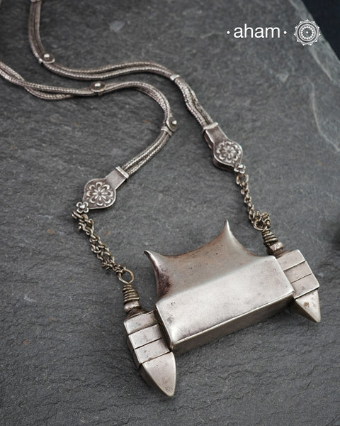 This handcrafted silver neckpiece features a revered Shiva lingam design, rooted in the spiritual traditions of the Lingayat community. The piece showcases meticulous artisanal craftsmanship, with its distinctive projection elegantly referencing Nandi, the sacred bull. Historically significant among Shaivite practitioners, particularly from Karnataka, this vintage-inspired silver casket serves as both a devotional ornament and cultural emblem. 