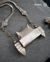 This handcrafted silver neckpiece features a revered Shiva lingam design, rooted in the spiritual traditions of the Lingayat community. The piece showcases meticulous artisanal craftsmanship, with its distinctive projection elegantly referencing Nandi, the sacred bull. Historically significant among Shaivite practitioners, particularly from Karnataka, this vintage-inspired silver casket serves as both a devotional ornament and cultural emblem. 