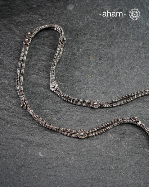 This handcrafted silver neckpiece features a revered Shiva lingam design, rooted in the spiritual traditions of the Lingayat community. The piece showcases meticulous artisanal craftsmanship, with its distinctive projection elegantly referencing Nandi, the sacred bull. Historically significant among Shaivite practitioners, particularly from Karnataka, this vintage-inspired silver casket serves as both a devotional ornament and cultural emblem. 