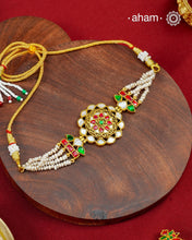 Crafted in 92.5 sterling silver with a luxurious&nbsp;&nbsp;gold polish, this handcrafted choker beautifully showcases the timeless elegance of traditional kundan artistry. At its heart lies an intricately detailed floral medallion, accented with luminous mother of pearl, vibrant ruby and emerald-toned stones, and delicate kundan work. Multiple strands of freshwater pearls on either side lend the piece a graceful, refined finish.