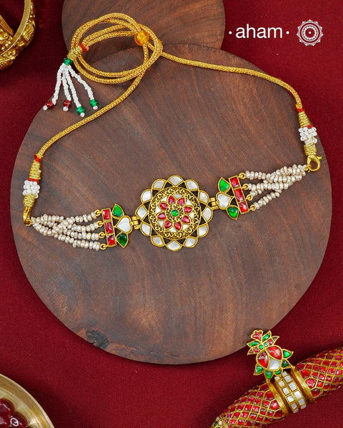 Crafted in 92.5 sterling silver with a luxurious&nbsp;&nbsp;gold polish, this handcrafted choker beautifully showcases the timeless elegance of traditional kundan artistry. At its heart lies an intricately detailed floral medallion, accented with luminous mother of pearl, vibrant ruby and emerald-toned stones, and delicate kundan work. Multiple strands of freshwater pearls on either side lend the piece a graceful, refined finish.
