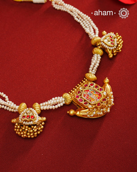 This exquisite neckpiece features 3 silver amulets with a gold polish finish, elegantly strung with lustrous pearls. At its center, the amulet showcases a finely hand-painted miniature depiction of Shrinathji, combining traditional craftsmanship with artistic detail. A distinguished piece that reflects devotion and timeless beauty.