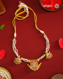 This exquisite neckpiece features 3 silver amulets with a gold polish finish, elegantly strung with lustrous pearls. At its center, the amulet showcases a finely hand-painted miniature depiction of Shrinathji, combining traditional craftsmanship with artistic detail. A distinguished piece that reflects devotion and timeless beauty.