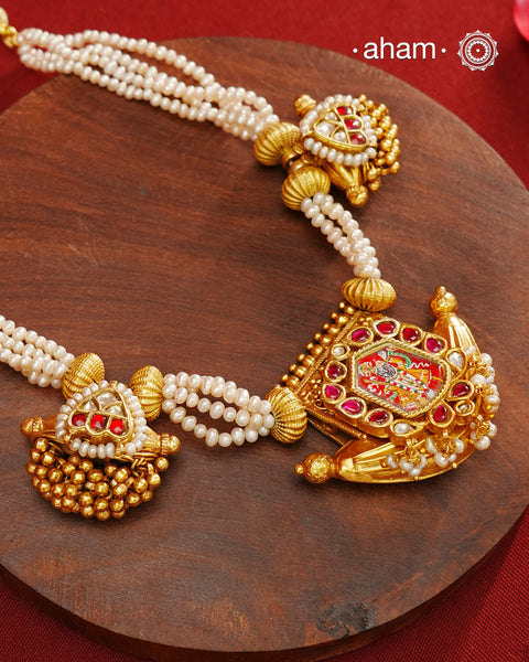 This exquisite neckpiece features 3 silver amulets with a gold polish finish, elegantly strung with lustrous pearls. At its center, the amulet showcases a finely hand-painted miniature depiction of Shrinathji, combining traditional craftsmanship with artistic detail. A distinguished piece that reflects devotion and timeless beauty.