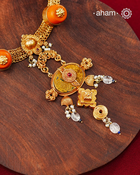 Crafted in 92.5 sterling silver with a radiant 24 carat gold polish, this handcrafted neckpiece brings together traditional craftsmanship and contemporary elegance. The intricately woven chain is accented with vibrant coral-toned beads, delicate freshwater pearl clusters, and an ornate statement pendant featuring intricate hand-finished detailing. Soft faceted natural stone drops add a graceful touch, lending subtle movement and refined charm to the design.