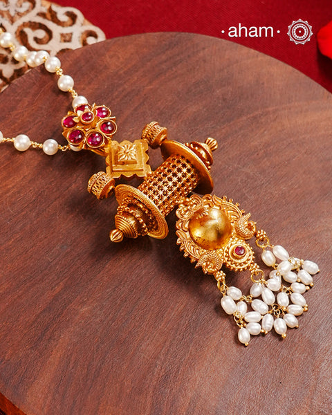 Inspired by the intricate designs of South temple art, this neckpiece is expertly crafted from 92.5% pure silver and finished with a refined dull gold polish. Complemented by a delicate pearl chain, it embodies a harmonious blend of traditional craftsmanship and timeless elegance, ideal for enhancing any special occasion ensemble.