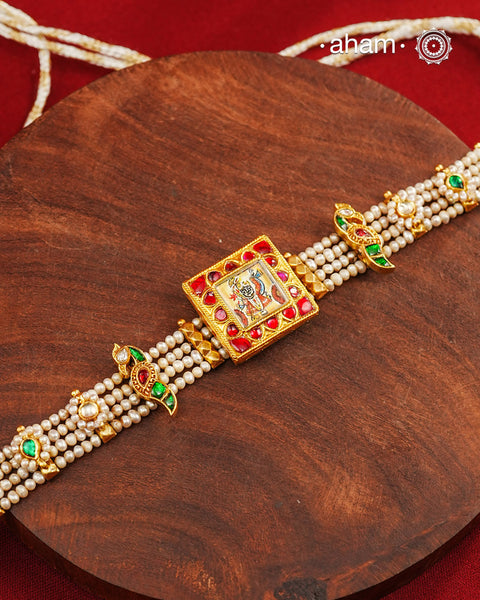 A delicate pearl choker set, thoughtfully designed with a hand-painted miniature of Shrinathji at its centre, accented with subtle kundan highlights. Crafted in 92.5 silver with a rich gold polish finish, this piece beautifully blends devotion, artistry and timeless elegance, making it perfect for festive occasions and heirloom-inspired styling.