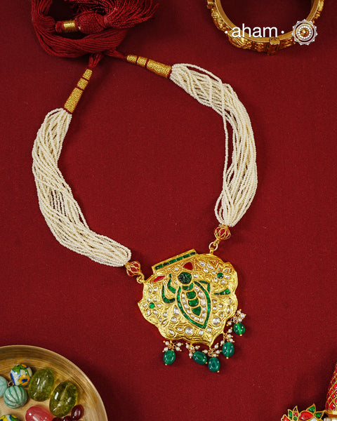 Crafted in 92.5 sterling silver with a radiant 24 carat gold polish, this handcrafted neckpiece draws inspiration from the divine adornments of Shrinathji. The intricately detailed pendant is embellished with traditional kundan work, vibrant emerald and ruby-toned accents, and graceful pearl detailing, while rich green stone drops add a striking finish. Multiple strands of delicate faux pearls complete the design, lending it an elegant and regal presence.