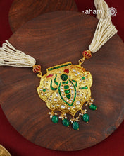 Crafted in 92.5 sterling silver with a radiant 24 carat gold polish, this handcrafted neckpiece draws inspiration from the divine adornments of Shrinathji. The intricately detailed pendant is embellished with traditional kundan work, vibrant emerald and ruby-toned accents, and graceful pearl detailing, while rich green stone drops add a striking finish. Multiple strands of delicate faux pearls complete the design, lending it an elegant and regal presence.
