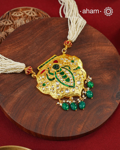 Crafted in 92.5 sterling silver with a radiant 24 carat gold polish, this handcrafted neckpiece draws inspiration from the divine adornments of Shrinathji. The intricately detailed pendant is embellished with traditional kundan work, vibrant emerald and ruby-toned accents, and graceful pearl detailing, while rich green stone drops add a striking finish. Multiple strands of delicate faux pearls complete the design, lending it an elegant and regal presence.