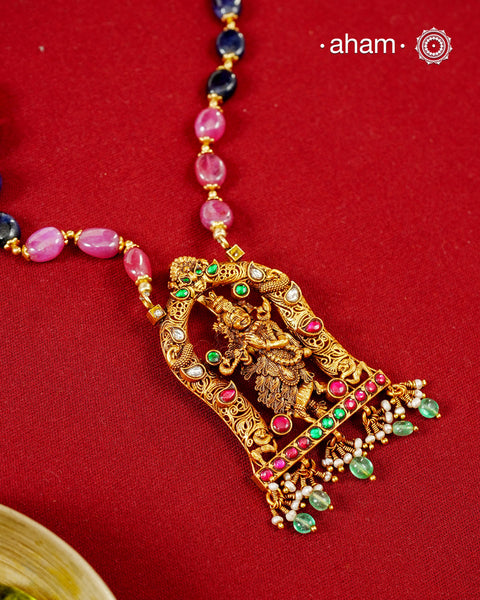 A graceful celebration of devotion and traditional craftsmanship, this necklace is handcrafted in 92.5 sterling silver and finished with a radiant gold polish. At its heart is an intricately sculpted Lord Krishna playing the flute, framed within an ornate temple arch adorned with kundan stones and vibrant ruby and emerald-toned accents.

The pendant is suspended from a colourful strand of natural multi-coloured semi-precious stone beads,
