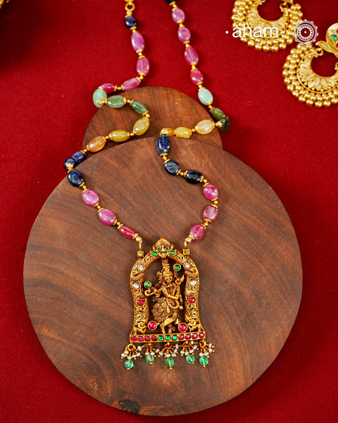 A graceful celebration of devotion and traditional craftsmanship, this necklace is handcrafted in 92.5 sterling silver and finished with a radiant gold polish. At its heart is an intricately sculpted Lord Krishna playing the flute, framed within an ornate temple arch adorned with kundan stones and vibrant ruby and emerald-toned accents.

The pendant is suspended from a colourful strand of natural multi-coloured semi-precious stone beads,