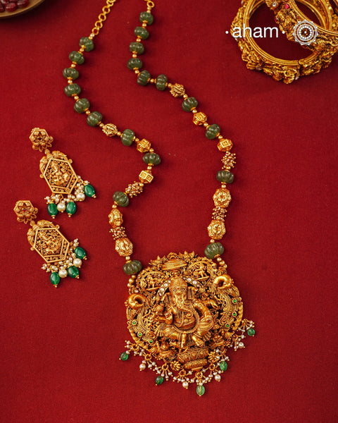 A magnificent tribute to South Indian temple jewellery, this handcrafted necklace is crafted in 92.5 sterling silver and finished with a rich gold polish. At its heart sits Lord Ganesha, intricately sculpted in a grand pendant that symbolises wisdom, protection, and auspicious beginnings.

Surrounded by elaborate nakshi work, traditional temple motifs, and graceful peacock details, the pendant showcases exceptional craftsmanship and attention to detail. Emerald-toned stone 
