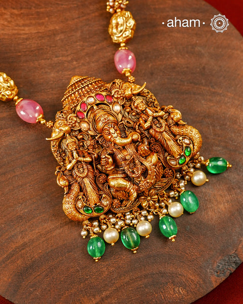 A magnificent expression of devotion and craftsmanship, this statement necklace is handcrafted in 92.5 sterling silver and finished with a rich gold polish. The intricately sculpted pendant features Lord Ganesha seated at the centre with Ridhi &amp; Sidhi on either side standing beneath an ornate temple canopy, symbolising wisdom, protection, and auspicious beginnings.