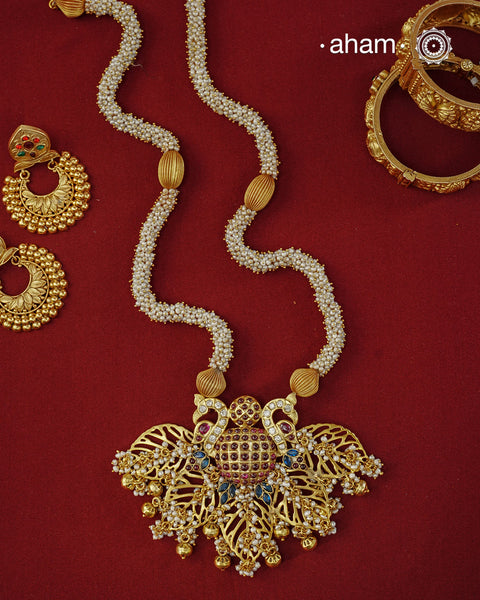 Crafted in 92.5 sterling silver with an opulent&nbsp;gold polish, this handcrafted neckpiece is a striking celebration of Indian artistry. A magnificent statement pendant, adorned with shimmering kundan work, vibrant ruby and sapphire-toned stones, and delicate pearl embellishments, is beautifully suspended from multiple strands of handwoven freshwater pearls. Intricate openwork detailing and graceful dangling accents add depth, movement, and timeless elegance to the design.