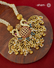 Crafted in 92.5 sterling silver with an opulent&nbsp;gold polish, this handcrafted neckpiece is a striking celebration of Indian artistry. A magnificent statement pendant, adorned with shimmering kundan work, vibrant ruby and sapphire-toned stones, and delicate pearl embellishments, is beautifully suspended from multiple strands of handwoven freshwater pearls. Intricate openwork detailing and graceful dangling accents add depth, movement, and timeless elegance to the design.