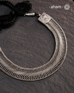 This Tribal Flat Silver Neckpiece features intricate wire weaving that contours elegantly around the neck. Crafted from high-quality silver, its timeless design complements both Indian traditional attire and contemporary western outfits, making it a versatile addition to any jewellery collection.
