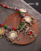 This Tribal Silver Neckpiece is a captivating blend of vintage charm and skilled craftsmanship. Featuring a central amulet with a delicate glass drop, it is beautifully complemented by four coin-shaped amulets stamped with intricate peacock motifs, two on each side. Carefully threaded together and crafted in silver, this unique piece adds a timeless, elegant touch to your collection, perfect for those who value heritage and artistry in their jewellery.