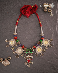 This Tribal Silver Neckpiece is a captivating blend of vintage charm and skilled craftsmanship. Featuring a central amulet with a delicate glass drop, it is beautifully complemented by four coin-shaped amulets stamped with intricate peacock motifs, two on each side. Carefully threaded together and crafted in silver, this unique piece adds a timeless, elegant touch to your collection, perfect for those who value heritage and artistry in their jewellery.