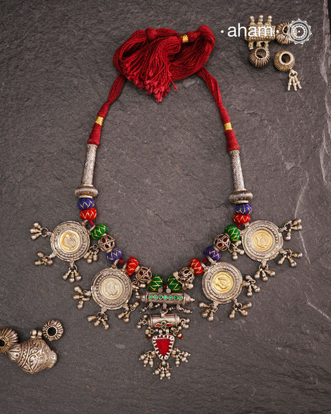 This Tribal Silver Neckpiece is a captivating blend of vintage charm and skilled craftsmanship. Featuring a central amulet with a delicate glass drop, it is beautifully complemented by four coin-shaped amulets stamped with intricate peacock motifs, two on each side. Carefully threaded together and crafted in silver, this unique piece adds a timeless, elegant touch to your collection, perfect for those who value heritage and artistry in their jewellery.