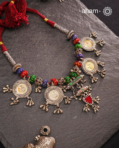 This Tribal Silver Neckpiece is a captivating blend of vintage charm and skilled craftsmanship. Featuring a central amulet with a delicate glass drop, it is beautifully complemented by four coin-shaped amulets stamped with intricate peacock motifs, two on each side. Carefully threaded together and crafted in silver, this unique piece adds a timeless, elegant touch to your collection, perfect for those who value heritage and artistry in their jewellery.