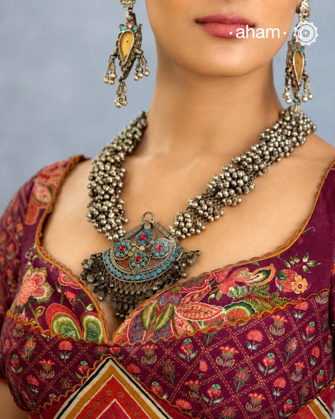 This Tribal Silver Neckpiece features a stunning pendant that was originally a headpiece complemented by tribal chains with multiple ghungroos for added drama. A true treasure for any jewellery lover.